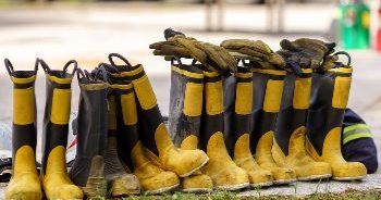 a lineup of firefighting boots with gloves placed on top of boots