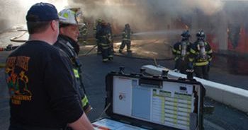 A group of firefighters near a smoky area. A few firefighters are using a hose.