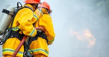 Two firefighters using a fire hose to put out a fire.